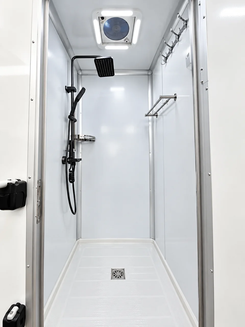 Private shower stall inside a shower trailer with overhead and handheld shower heads, ventilation and storage hooks